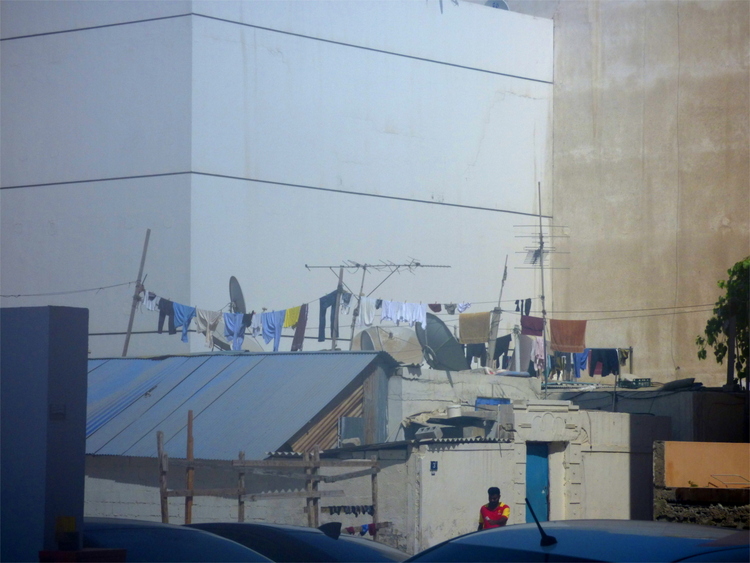 Clothes hanging out to dry on the roof of a low sandstone-coloured building surrounded by taller buildings
