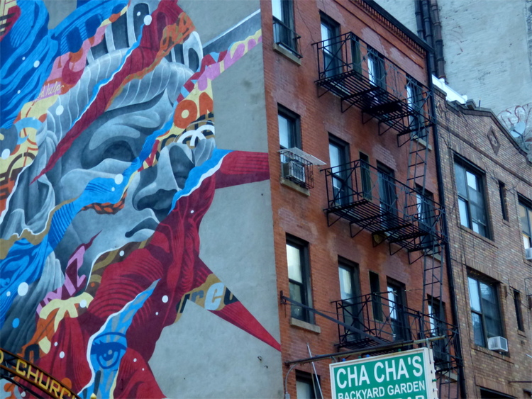 A mural showing a colourful patterned impression of the statue of liberty on one side of a red brick building