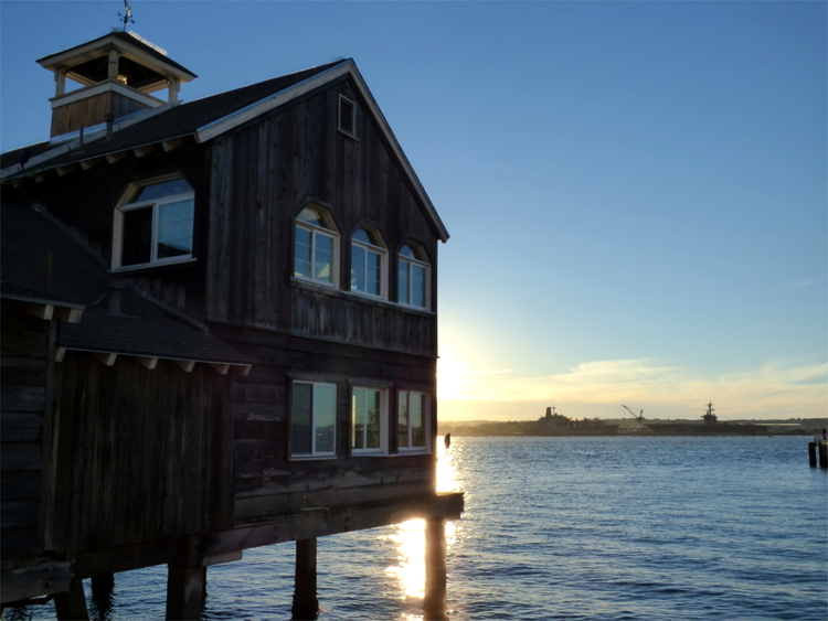 The sun setting above the ocean behind a wooden house built on stakes in the water