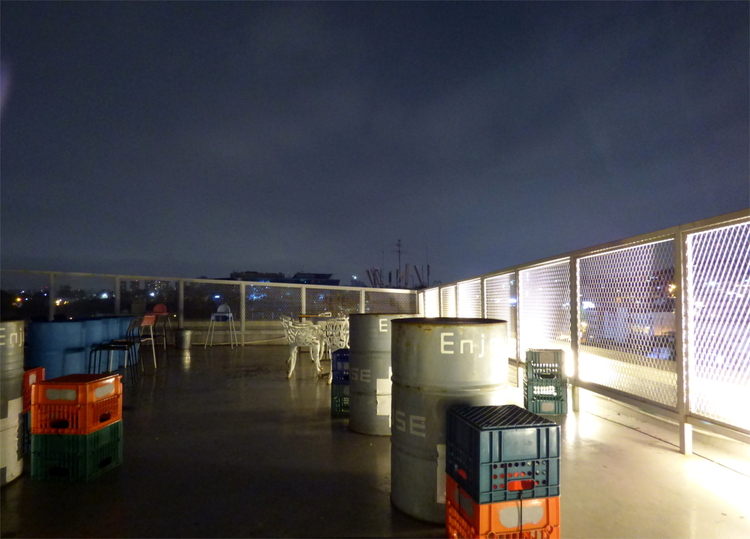Steel barrels and beverage crate arranged into tables and chairs on a rooftop terrace