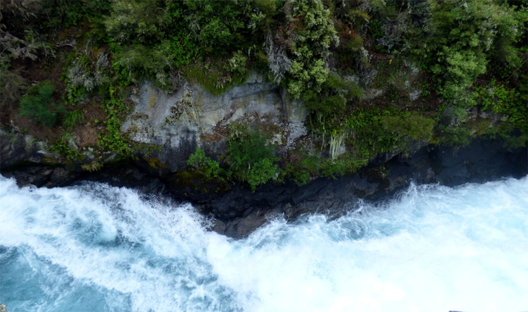 A wild, foamy white river running through a mossy rock channel