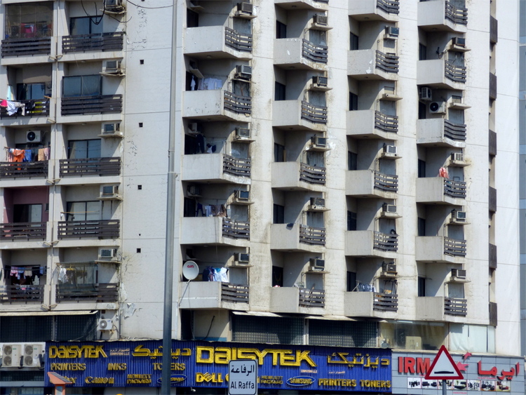 Beige facade of an apartment building with neon signs of businesses on the ground floor