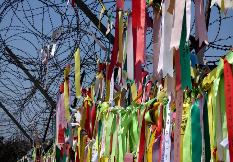 Fabric ribbons with messages written on them tied to a barbed wire fence