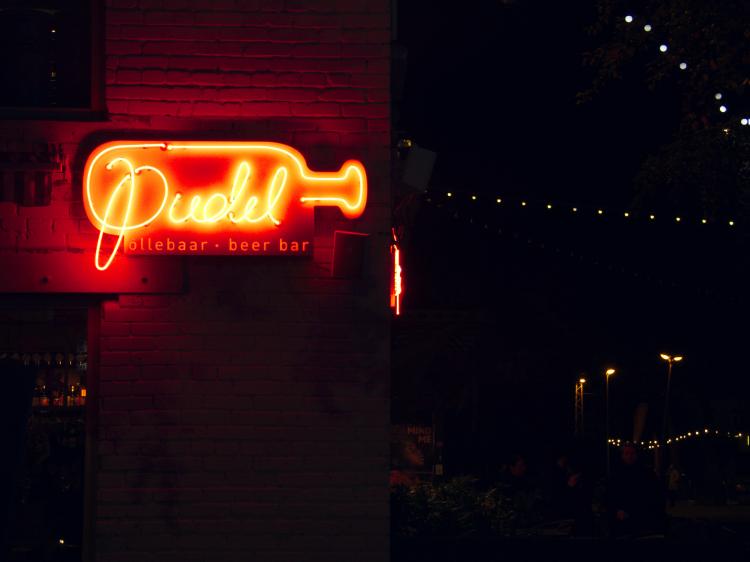 A red neon sign reading 'Pudel' in a hand-written font inside a stylized bottle