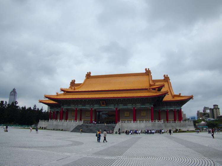 A large, palace-like building with an arching orange roof on a large square with geometric lines on the ground