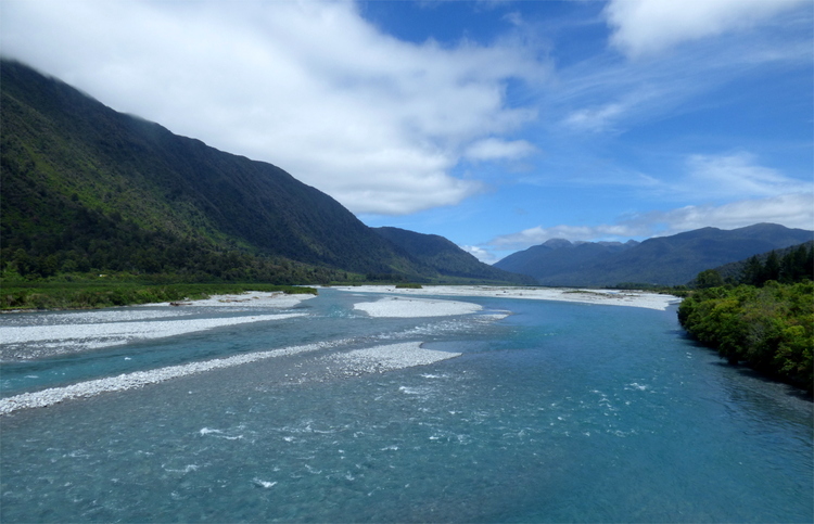 A broad river running through a white gravel bed enclosed by green hills