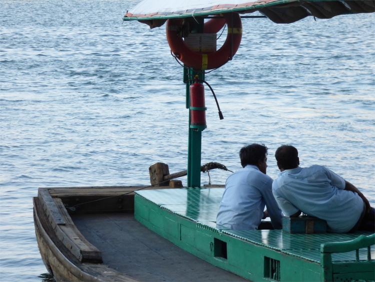 Two men leaning towards each other on a green wooden boat on the water