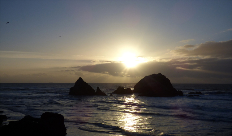 The sun setting over some rocks in the ocean