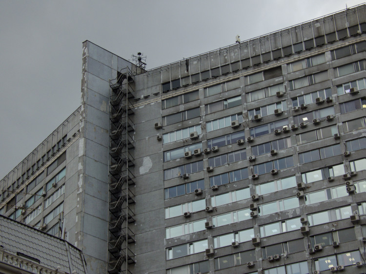 Facade of a huge grey concrete building with countless windows and AC units in random places