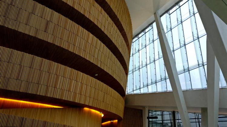 A large glass window front on the right meets round, multi-story wooden walkways on the left as some angled white pillars cross into view supporting an unseen ceiling.
