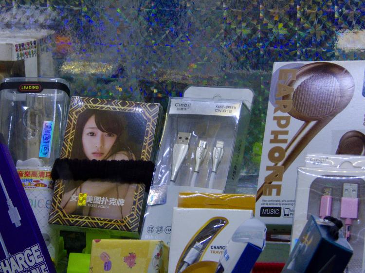 The inside of a claw-machine with various packages containing charging cables as well as a pornographic playing card set with a woman looking seductively into the camera on the outside