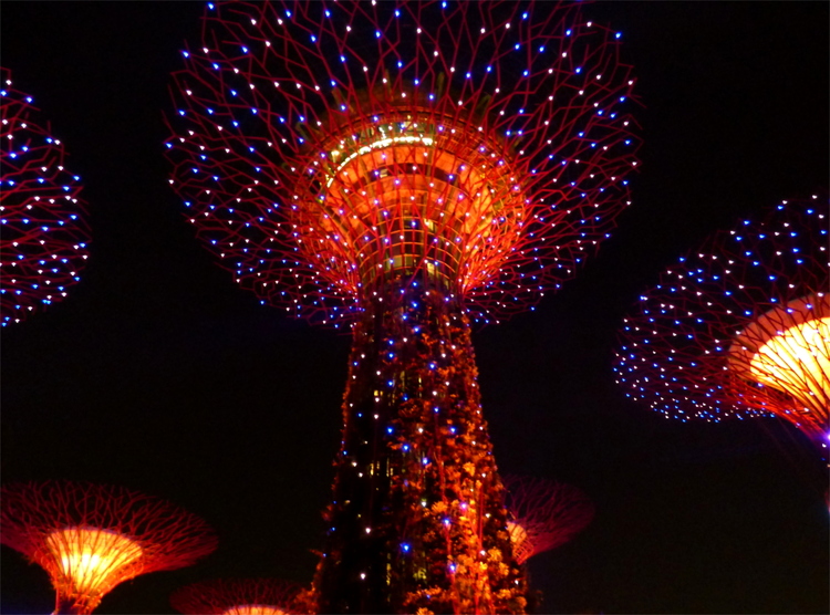Artificial tree structures overgrown with plants and many interspersed lights, lit in deep red