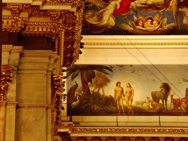 A fresco in a gold-adorned church showing Adam and Eve standing next to each other, nude, with some animals in a tropical landscape