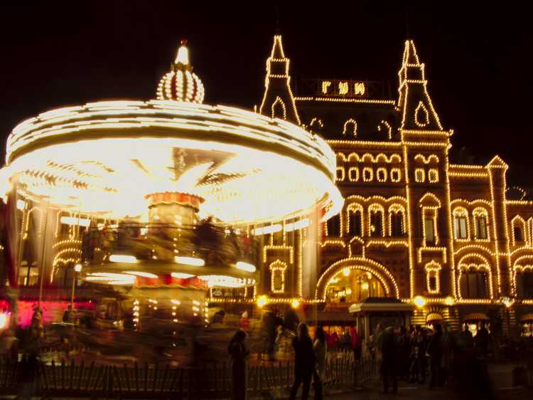 A brightly lit carousel spinning in front of a large building outlined in lights