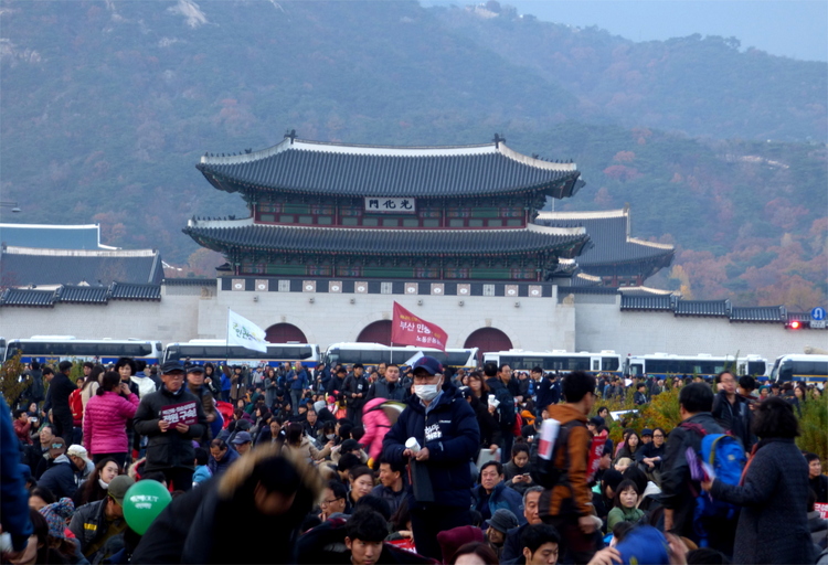 A dense crowd of protestors in front of the arched roofs of a old city gate
