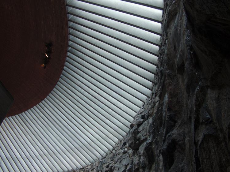 Light falling in through radial slits in a concrete ceiling of a round, cave-like rough rock room