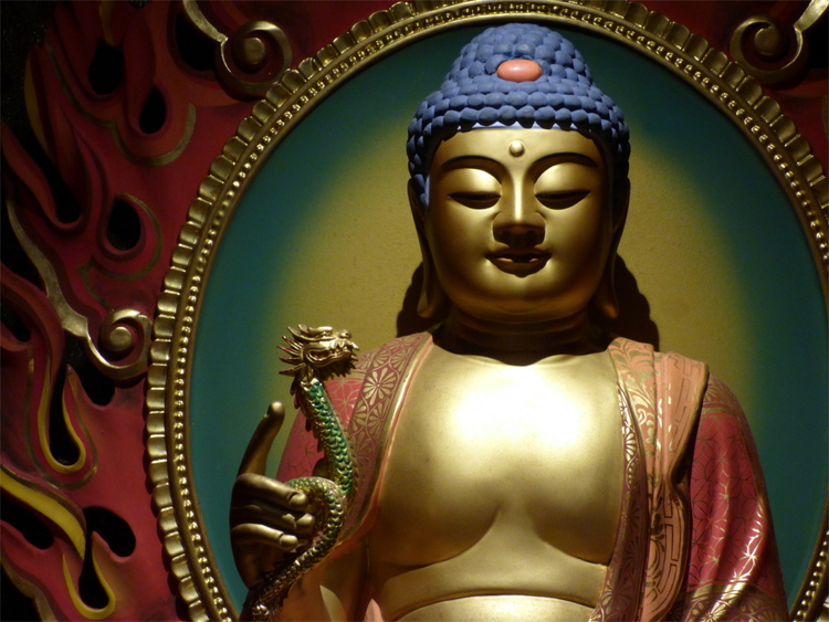 A painted golden Buddha statue holding a snake, surrounded by stylized flames in the background