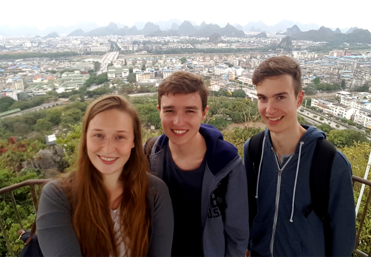Katha, Jan and Nils posing for a group picture on a mountain with a city in the background